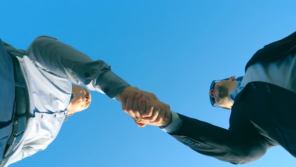 Young Salesman in Formal Suit Greeting with Male Buyer and Giving Him Keys of Car on the Blue Sky