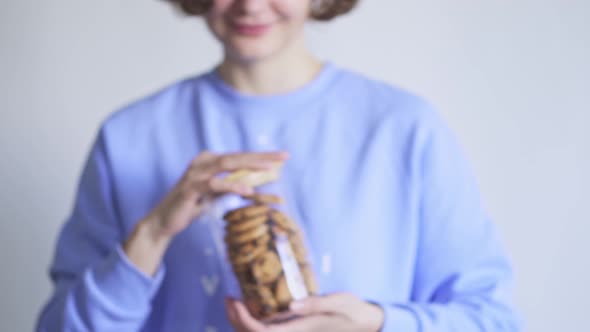 A Glass Jar Full Of Homemade Chocolate Chip Cookies. A Girl In A Blue Sweater Holds Out 
