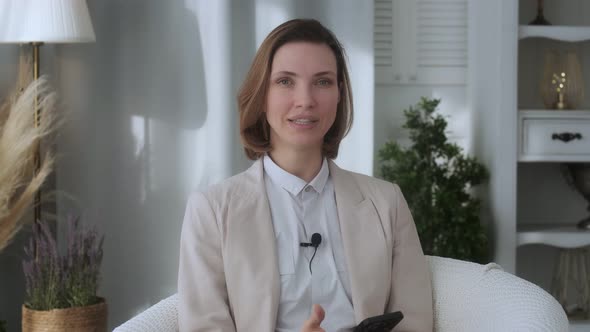 Smiling young woman, blogger, vlogger, influencer, sitting at home, talking, looking at the camera