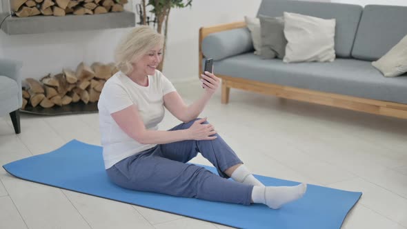 Old Woman Talking on Video Call on Smartphone While Sitting on Yoga Mat