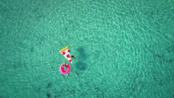 Close aerial view of two young girls swimming and playing in sea with inflatables.