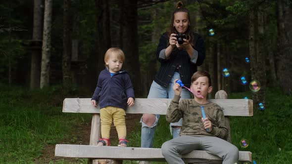 Young mother with her sons playing with soap bubbles and makes pictures on the camera in the park.