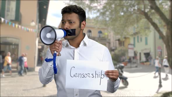 Man with Taped Mouth Trying to Speak Into Megaphone