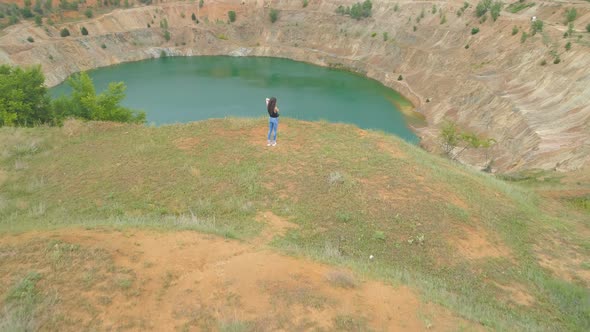 Young Woman Standing on Cliff Edge and Looking at Abandoned Copper Mine Pit Partially Full of Blue