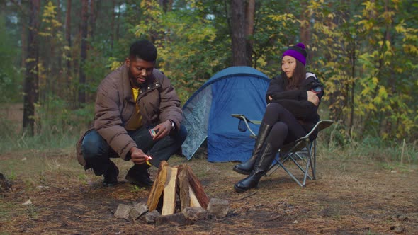 Hiker Man Kindling Campfire To Warm Up in Evening