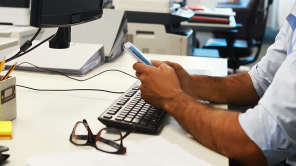 Male executive using mobile phone while working on computer