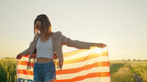 Confident Woman Waving Stars and Stripes USA Flag at Field at Sunset