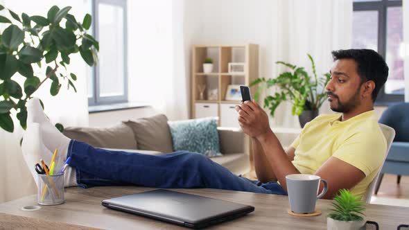 Indian Man with Smartphone Resting Feet on Table