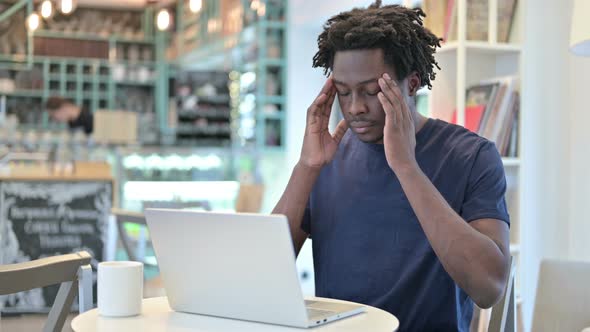 African Man with Headache Working on Laptop in Cafe