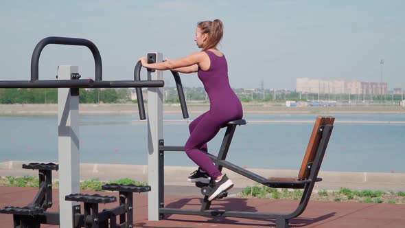 Slim Athletic Woman with Sexy Buttocks Exercise on Stationary Bike on Workout Ground in a City Park