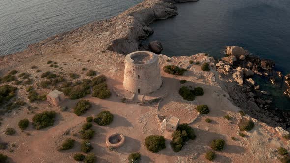 Pirate tower in Ibiza. Aerial view panning around lookout tower showing cliffs, ocean and tower duri