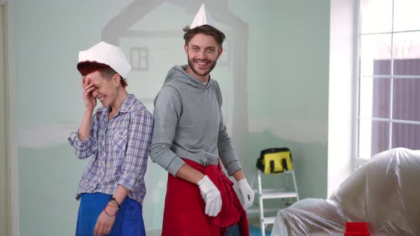 Zoom in to Cheerful Couple in Paper Hats Crossing Hands Posing in New House