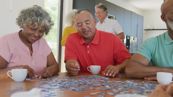 Happy senior diverse people playing puzzle at table at retirement home