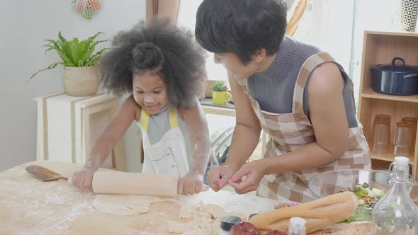 African America family with mother wearing apron rolling thresh flour for cooking with daughter.