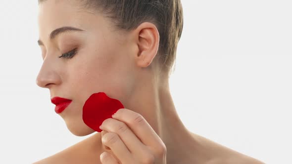 Beauty and Bright Red Lipstick on Lips. Pretty Woman Holds a Red Rose Petal on Her Cheekbone