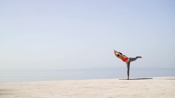Fit Female Doing Yoga Asanas on Stone Paving with Sea and Sky on Background