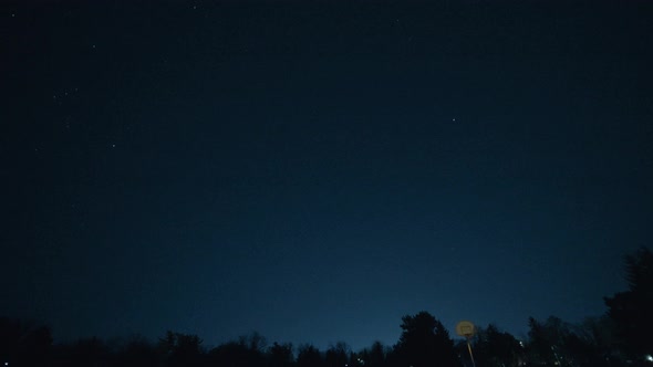 Shooting star passes through the sky over an empty basketball court at night.