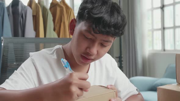 Close Up Of Asian Man Online Seller Writing On Package While Selling Clothes At Home