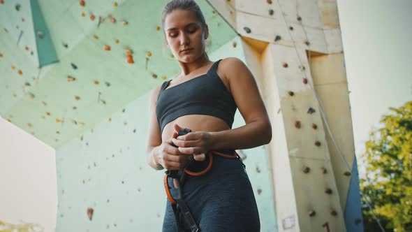 Young Woman Putting on Belaying Harness Preparing for Climbing Practice