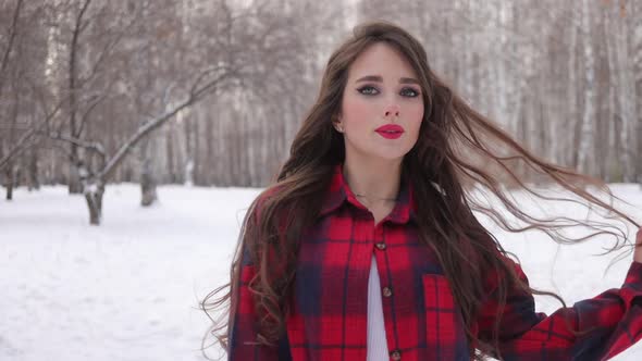 Young Woman with Wavy Hair Standing and Touching Face in Winter Forest