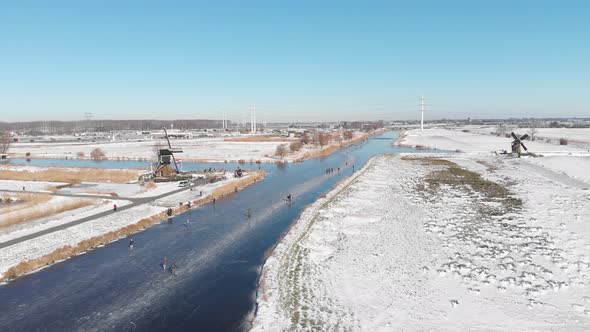 Netherlands winter, locals ice skating on frozen canal near windmill aerial view