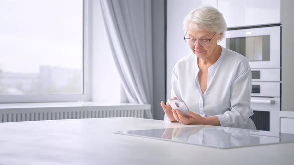 Lady pensioner with short grey hair and glasses surfs internet on smartphone