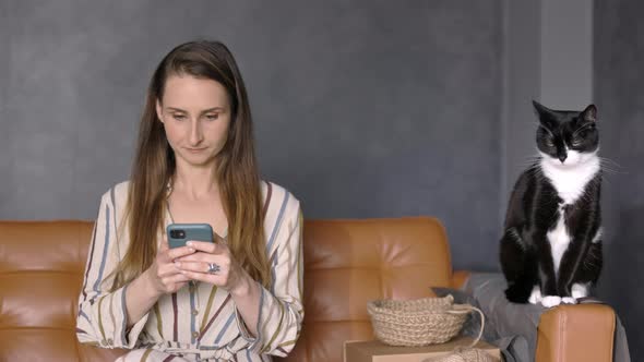 Woman Holding a Smartphone sitting on the Couch with her Cat and Working from Home, Copy Space