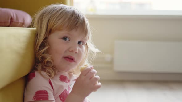 Close Up Little Cheerful Girl Child in Pink Dress Sits on Floor in Living Room Next to Yellow Sofa