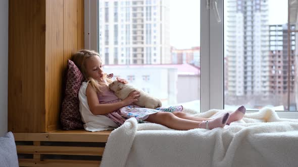 Little Girl Sitting on Windowsill with Puppy