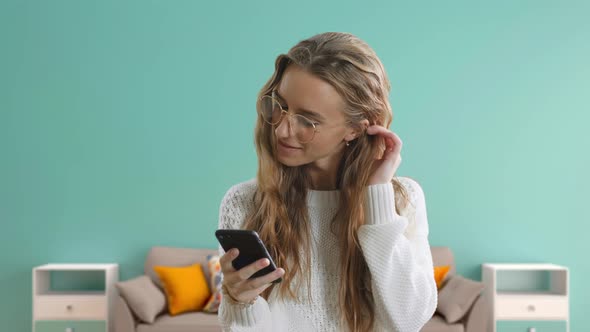 Pretty Young Woman Wearing Stylish Glasses Is Holding a Smart Phone, Using a Smartphone and Smiling