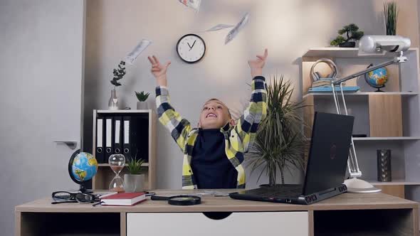 Smiling Handsome 10-Aged Schoolboy Scattering Money Over His Head, Sitting at the Table at Home