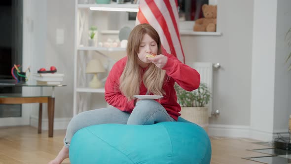 Relaxed Korean Teen Girl Watching TV and Eating Pizza Sitting on Bag Chair Indoors