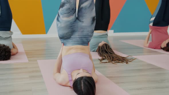 Attractive Slender Women Doing Yoga in Studio Laying on Mats with Legs Up Wearing Sportswear