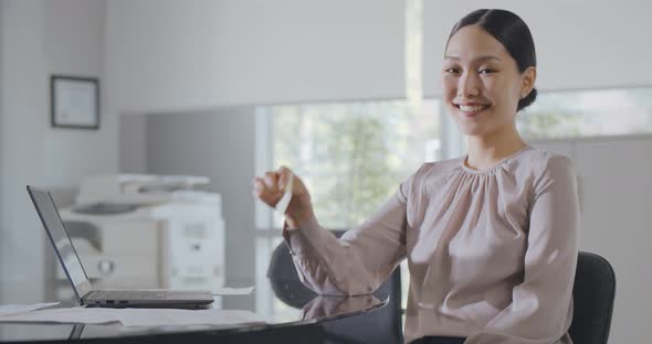 Medium Shot of Asian Businesswoman Looking at Camera and Holding Upset Smile Sticker By Her Mouth