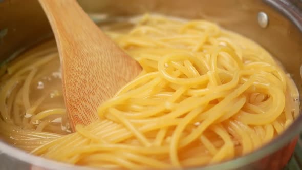 Raw spaghetti is being cooked in boiling water in a kitchen pot.