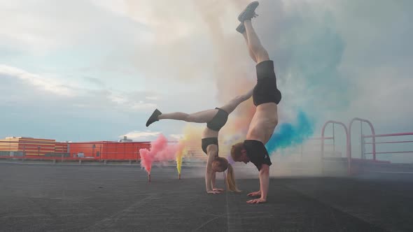 Slow Motion Female and Man Doing a Handstands Man Makes a Flips Multi Colored Smoke Bombs on a
