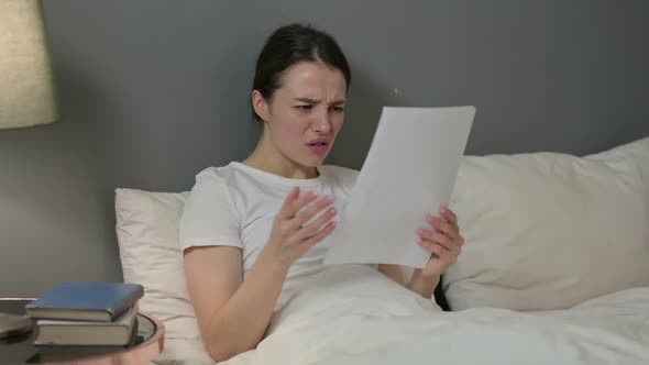 Young Woman Reacting to Loss on Documents in Bed