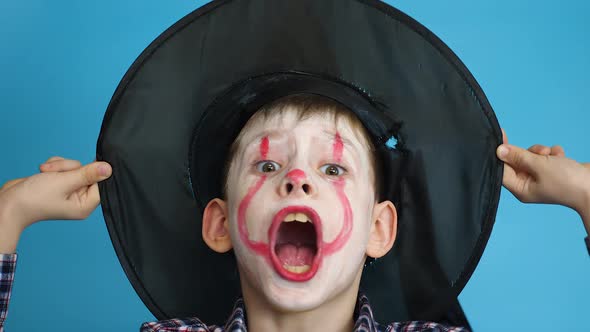 portrait of a caucasian boy 7-8 years old in a carnival make-up of a scary monster in a hat looking 