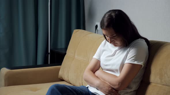 Young Woman Hunched Over Holding Belly While Sitting on the Couch