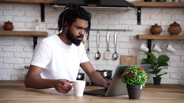Young modern African American man with dreadlocks is drinking coffee while working 
