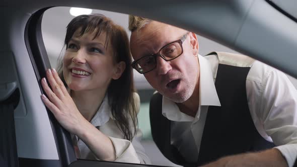 Shooting From Car Salon of Positive Adult Successful Caucasian Couple Talking Choosing New Vehicle