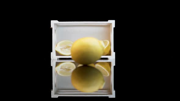 A lemon rolling towards a white crate with three halves of lemons
