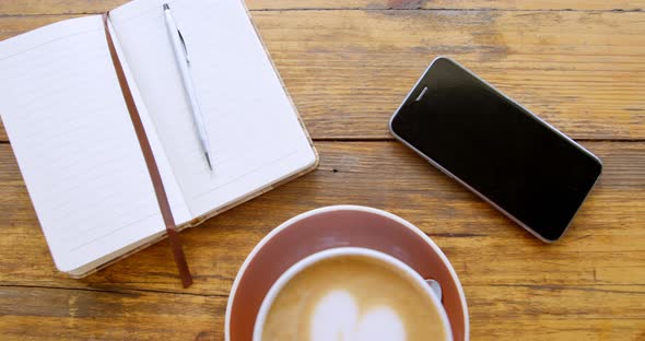 Cup of hot coffee latte with heart shaped foam art with diary and mobile phone