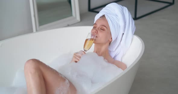 Charming Delighted Woman Declining in Bubble Bathtub Enjoying Spa Day Drinking White Sparkling Wine
