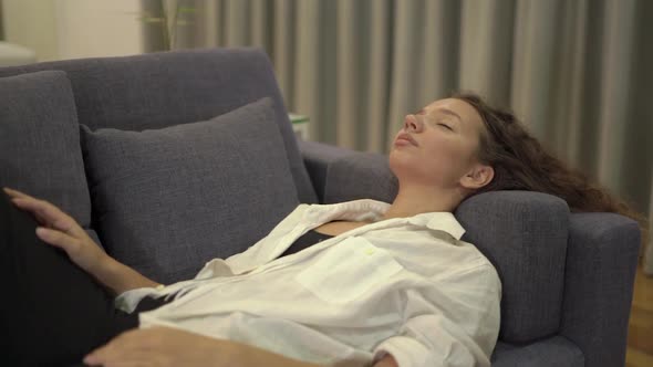 Tired Mixed Race Young Woman Lies on Grey Sofa with Pillows