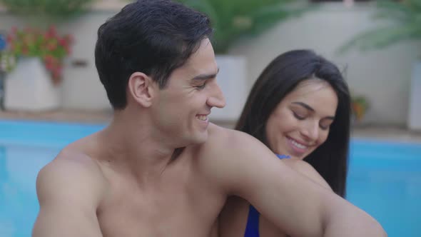 Handsome man turns and smiles to young attractive girlfriend by swimming pool