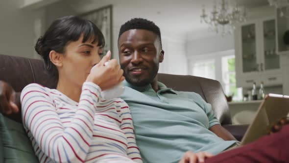 Happy diverse couple sitting on couch and drinking coffee in living room