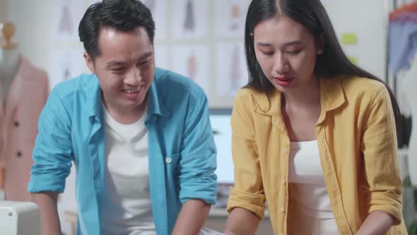 Asian Male And Female Designers Helping Each Other Rearrange The Papers While Designing Clothes