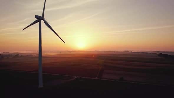 Silhouette of Wind Turbine in Farm Fields with Bright Orange Rising Sun in Background