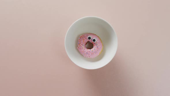 Video of donut with icing on white plate over pink background